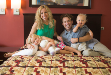 Mom, dad and two kids smiling while laying on a bed