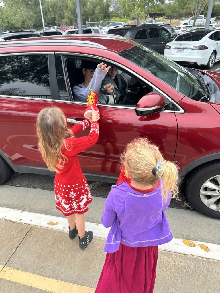 People in a car putting money in a red boot held by an elementary school aged girl
