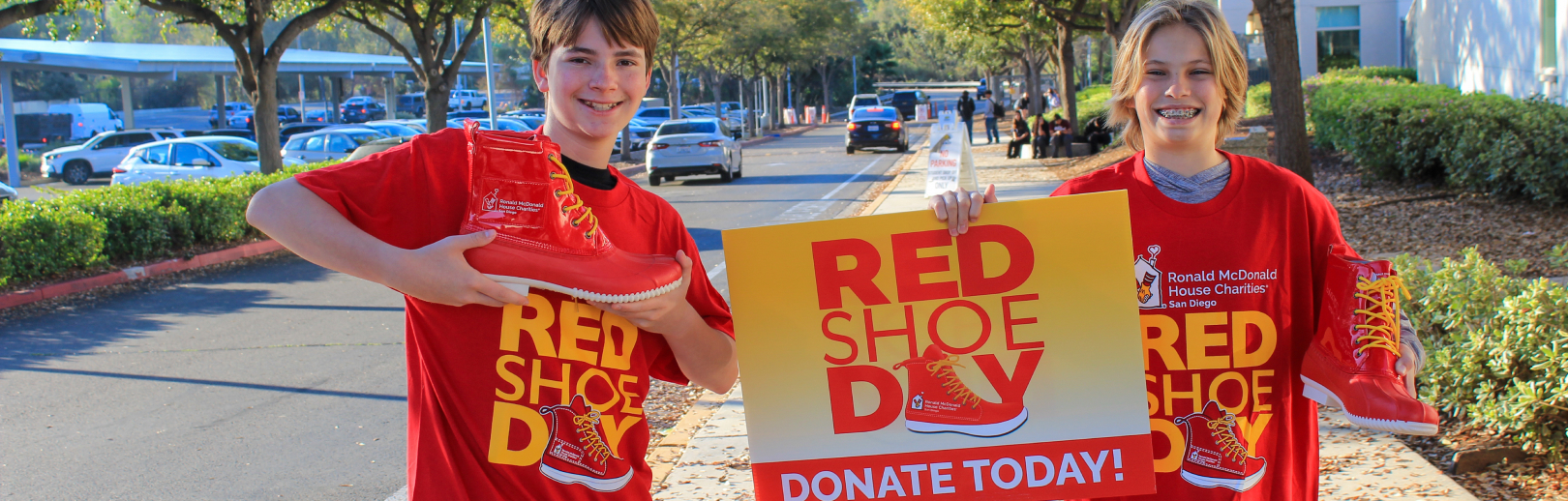 two smiling middle school boys holding red boots and a Red SHoe Day sign