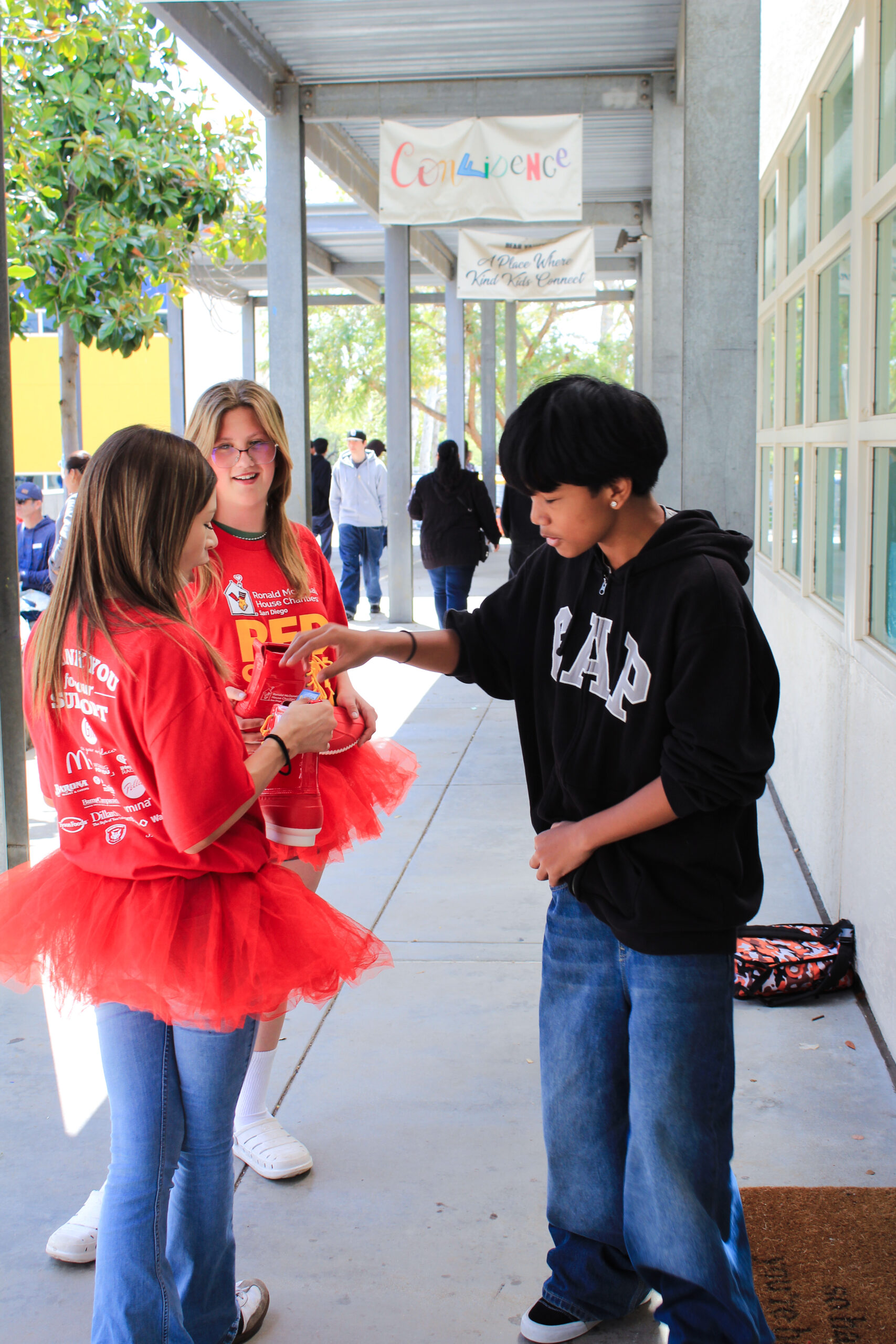 A middle school aged boy putting money in a red shoe held by a girl