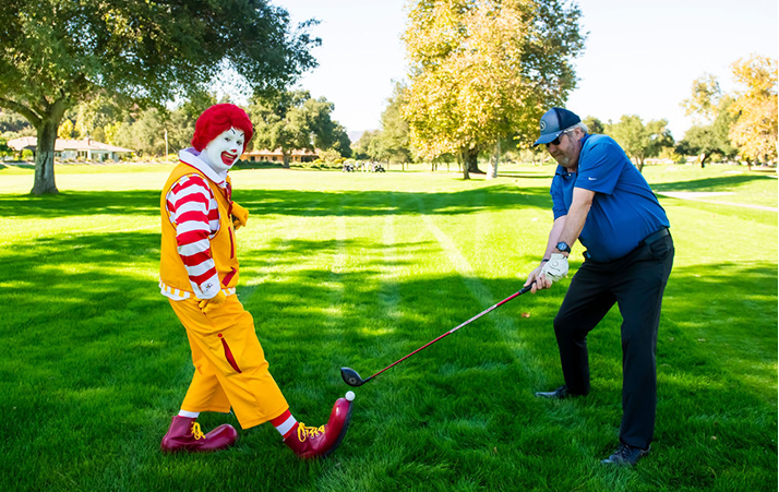 ronald mcdonald using shoe as a gold tee