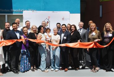group of people holding a ribbon and girl cutting it