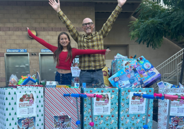 two volunteers standing behind toys they collected